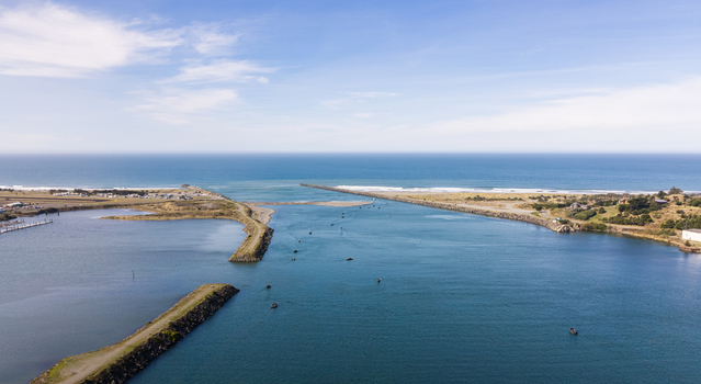 Aerial view of salmon fishing boats navigating the river mouth at the Pacific Ocean coastline in Gold Beach Oregon United States.