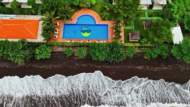 Aerial view of a resort pool near a black sand beach Indonesia.