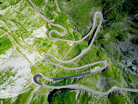 Aerial view of the winding Transfagarasan mountain road with sharp hairpin turns cutting through the lush green slopes of the Carpathian Mountains Curtea de Arges Judetul Arges Romania. Aerial view of the winding Transfagarasan mountain road with sharp hairpin turns cutting through the lush green slopes of the Carpathian Mountains Curtea de Arges Judetul Arges Romania.