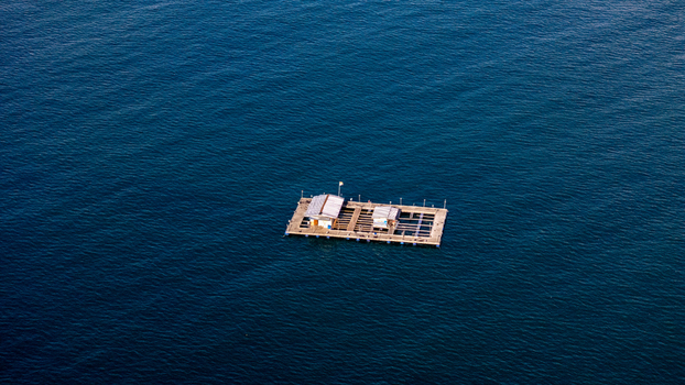 Aerial view of a floating fish farm platform on the calm blue waters of Pantai Karanggongso in Watulimo East Java Indonesia. Aerial view of a floating fish farm platform on the calm blue waters of Pantai Karanggongso in Watulimo East Java Indonesia.