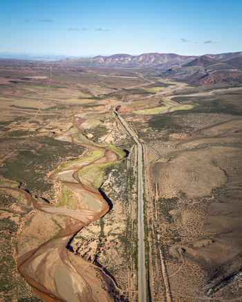 Aerial view of a winding river and a straight road cutting through the arid landscape of the Argentine desert under a clear blue sky Argentina. Aerial view of a winding river and a straight road cutting through the arid landscape of the Argentine desert under a clear blue sky Argentina.