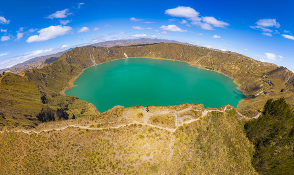 Aerial view of Quilotoa Lake with its vibrant turquoise water inside a volcanic caldera surrounded by rugged mountain ridges under a bright blue sky in Quilotoa Cotopaxi Ecuador. Aerial view of Quilotoa Lake with its vibrant turquoise water inside a volcanic caldera surrounded by rugged mountain ridges under a bright blue sky in Quilotoa Cotopaxi Ecuador.