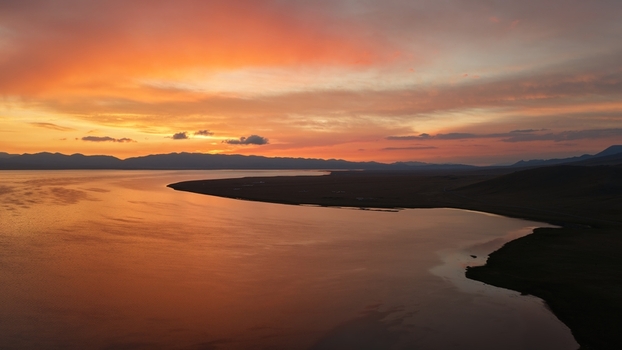 Aerial view of Song Kul lake at sunset with vibrant orange and pink sky reflecting on the calm water and surrounding mountains in Naryn Region Kyrgyzstan. Aerial view of Song Kul lake at sunset with vibrant orange and pink sky reflecting on the calm water and surrounding mountains in Naryn Region Kyrgyzstan.