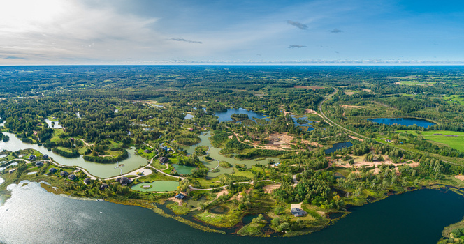 Aerial view of a scenic landscape featuring numerous interconnected lakes dense green forests and scattered residential houses under a clear blue sky in Latvia. Aerial view of a scenic landscape featuring numerous interconnected lakes dense green forests and scattered residential houses under a clear blue sky in Latvia.