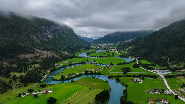 Aerial view of a winding river flowing through a lush green valley surrounded by steep mountains under a cloudy sky in Nordland Norway. Aerial view of a winding river flowing through a lush green valley surrounded by steep mountains under a cloudy sky in Nordland Norway.