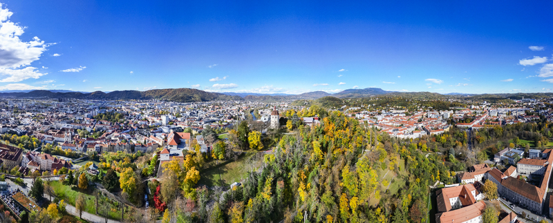 Aerial view of the vibrant autumn foliage surrounding the Schlossberg hill and cityscape under a clear blue sky Graz Styria Austria.