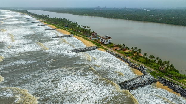 Aerial view of Mattu Beach featuring a narrow strip of land separating the Arabian Sea from the backwaters with stone breakwaters and palm trees in Udupi Karnataka India.