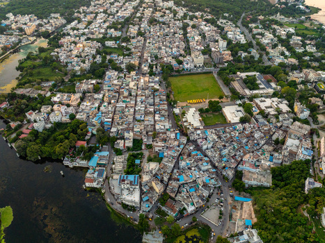 Aerial view of the dense urban landscape of Udaipur featuring traditional buildings narrow streets a green field and the serene waters of the lake in Udaipur Rajasthan India.