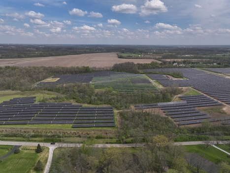 Lebanon United States 12 April 2026 Aerial view of a large solar panel farm surrounded by green fields and trees under a blue sky with white clouds.