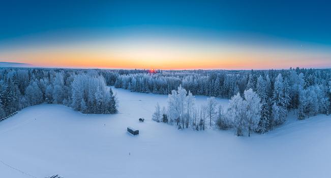 Aerial view of a snow covered forest landscape with frost covered trees and small wooden structures under a vibrant sunset sky in Latvia. Aerial view of a snow covered forest landscape with frost covered trees and small wooden structures under a vibrant sunset sky in Latvia.