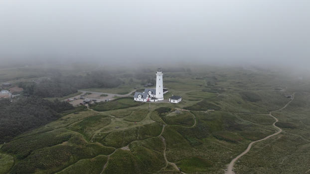 Aerial view of Hirtshals fyr surrounded by grassy dunes and rolling hills under a thick blanket of fog in Hirtshals Denmark. Aerial view of Hirtshals fyr surrounded by grassy dunes and rolling hills under a thick blanket of fog in Hirtshals Denmark.