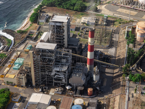 Aerial view of the industrial power plant with its red and white chimney piping and storage tanks along the coastline in Bajos de Haina San Cristobal Province Dominican Republic.