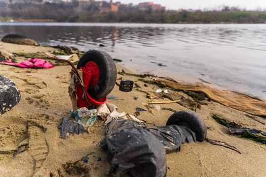 View of a discarded broken toy bicycle on the sandy shore of Lake Varna surrounded by plastic debris with calm water and distant shoreline in the background in Varna Bulgaria. View of a discarded broken toy bicycle on the sandy shore of Lake Varna surrounded by plastic debris with calm water and distant shoreline in the background in Varna Bulgaria.