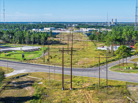 Aerial view of power lines crossing a road intersection near an industrial area with surrounding forest in Wilmington North Carolina United States.