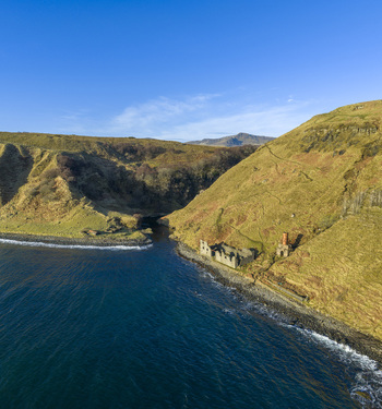Aerial view of Lealt Falls ruins on the rugged coastline with steep grassy cliffs and deep blue sea Isle of Skye Scotland United Kingdom. Aerial view of Lealt Falls ruins on the rugged coastline with steep grassy cliffs and deep blue sea Isle of Skye Scotland United Kingdom.