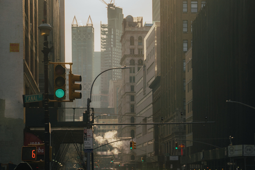 View of the busy Canal Street intersection with traffic lights steam rising from the street and surrounding skyscrapers in the golden afternoon light in New York New York United States.