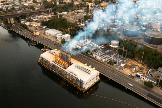 Aerial view of the Seaboard Transcontinental floating power plant emitting smoke on the Ozama River with urban surroundings in Santo Domingo Distrito Nacional Dominican Republic. Aerial view of the Seaboard Transcontinental floating power plant emitting smoke on the Ozama River with urban surroundings in Santo Domingo Distrito Nacional Dominican Republic.