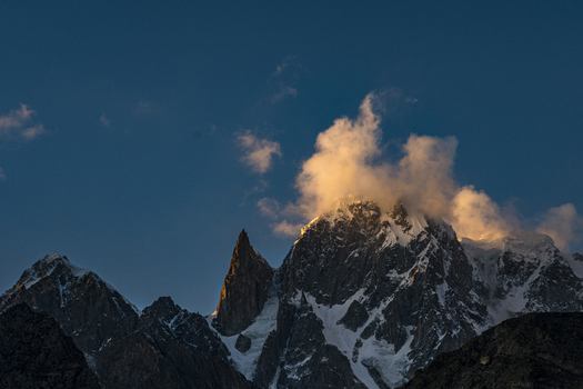 View of Lady Finger Peak illuminated by golden hour light with clouds clinging to the summit against a deep blue sky in Hunza Nagar Gilgit Baltistan Pakistan.