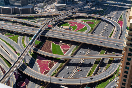 View of a complex multi level highway interchange with a metro train on tracks and landscaped flower beds in Dubai Dubai United Arab Emirates. View of a complex multi level highway interchange with a metro train on tracks and landscaped flower beds in Dubai Dubai United Arab Emirates.