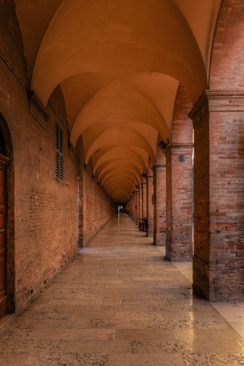 View of a long historic brick arcade with vaulted ceilings and stone flooring creating a symmetrical perspective leading into the distance in Urbino Marche Italy. View of a long historic brick arcade with vaulted ceilings and stone flooring creating a symmetrical perspective leading into the distance in Urbino Marche Italy.