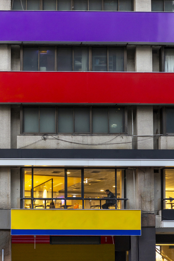 View of a modern building facade with vibrant purple red and yellow horizontal bands and a person visible through a lit window Taipei City Taiwan. View of a modern building facade with vibrant purple red and yellow horizontal bands and a person visible through a lit window Taipei City Taiwan.