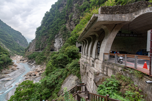 View of the road tunnel carved into the cliffside at Taroko National Park with a river flowing through the gorge below and lush green mountains in Xiulin Township Hualien County Taiwan.