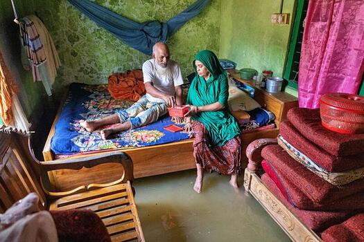Banshkhali Upazila Chittagong Division Bangladesh 10 July 2026 View of an elderly couple sitting on their bed inside a flooded home surrounded by rising water levels. Banshkhali Upazila Chittagong Division Bangladesh 10 July 2026 View of an elderly couple sitting on their bed inside a flooded home surrounded by rising water levels.