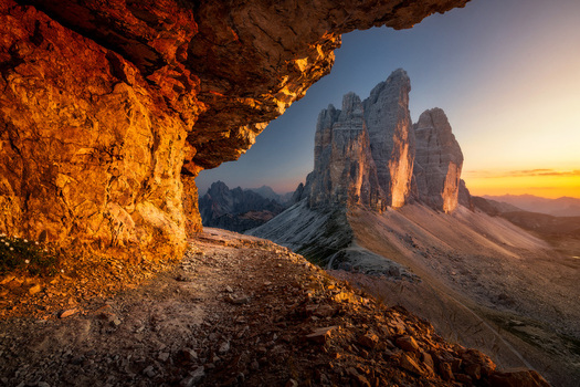 View of Tre Cime di Lavaredo peaks framed by a rocky cave opening during a vibrant sunset in Auronzo di Cadore Veneto Italy.