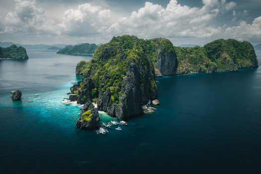 Aerial view of the limestone cliffs and turquoise waters of El Nido with traditional outrigger boats anchored near the shore in El Nido Mimaropa Philippines. Aerial view of the limestone cliffs and turquoise waters of El Nido with traditional outrigger boats anchored near the shore in El Nido Mimaropa Philippines.