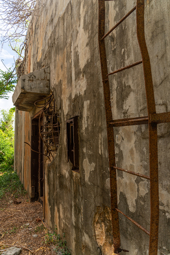 View of the weathered concrete wall of the historic North Field Base with a rusted metal ladder and exposed rebar in Northern Tinian Tinian Northern Mariana Islands. View of the weathered concrete wall of the historic North Field Base with a rusted metal ladder and exposed rebar in Northern Tinian Tinian Northern Mariana Islands.
