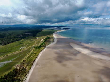 Aerial view of Moray Firth Coast featuring expansive sandy beaches lush green coastal vegetation and dark clouds casting shadows over the water in Nairn Scotland United Kingdom.