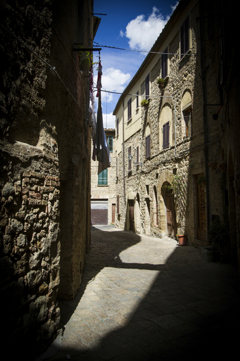 View of aged stone buildings casting long shadows in a narrow street clothes strung overhead under a bright sky Volterra Tuscany Italy. View of aged stone buildings casting long shadows in a narrow street clothes strung overhead under a bright sky Volterra Tuscany Italy.