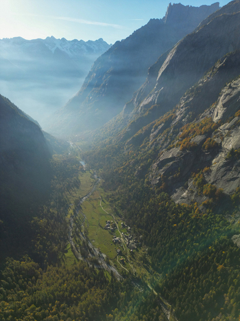 Aerial view of the Val di Mello valley with its steep granite cliffs winding river and autumn forests under a light morning mist in Val Masino Lombardia Italy. Aerial view of the Val di Mello valley with its steep granite cliffs winding river and autumn forests under a light morning mist in Val Masino Lombardia Italy.