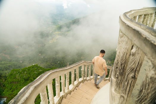 Sri Lanka 22 February 2026 View of a man walking down a spiral staircase with white railings overlooking a lush green valley covered in thick fog.