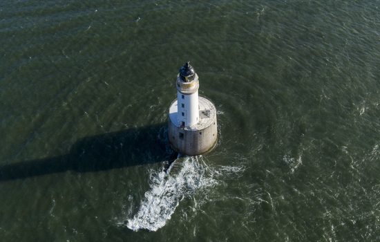 Aerial view of Rattray Head Lighthouse standing in the choppy North Sea with its long shadow cast on the dark green water Peterhead Scotland United Kingdom. Aerial view of Rattray Head Lighthouse standing in the choppy North Sea with its long shadow cast on the dark green water Peterhead Scotland United Kingdom.