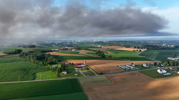 Rapho Township United States 05 July 2023 Aerial view of agricultural fields and farmsteads with a large plume of dark smoke drifting across the sky.