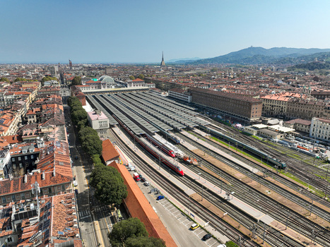 Aerial view of Porta Nuova railway station with trains on tracks historic city buildings and the Mole Antonelliana under a clear blue sky in Turin Piedmont Italy. Aerial view of Porta Nuova railway station with trains on tracks historic city buildings and the Mole Antonelliana under a clear blue sky in Turin Piedmont Italy.