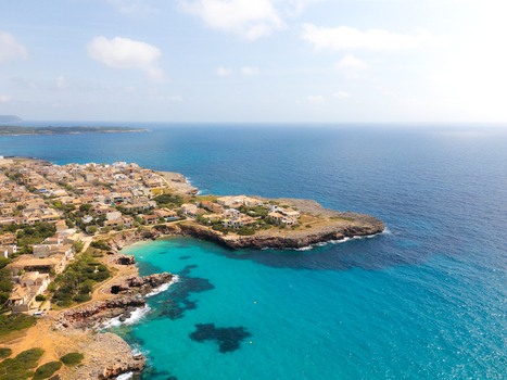 Aerial view of the turquoise waters and rocky coastline of the beach with residential buildings and lush vegetation under a bright sky Sa Coma Balearic Islands Spain. Aerial view of the turquoise waters and rocky coastline of the beach with residential buildings and lush vegetation under a bright sky Sa Coma Balearic Islands Spain.
