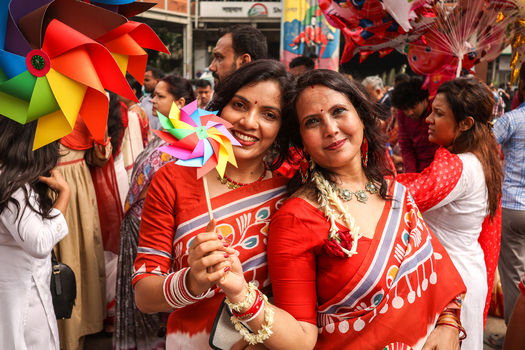 Dhaka Bangladesh 13 April 2026 View of joyful women adorned in vibrant red and white saris their radiant smiles and colorful pinwheels contrasting with the bustling festive street.
