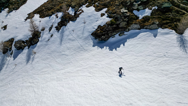 Aerial view of a lone skier traversing a snowy mountain slope near Pointe Ronde with rocky outcrops and scattered trees in Trient Valais Switzerland.