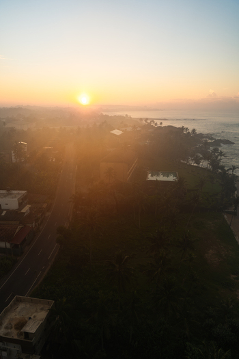 View of the coastal town at sunrise with hazy golden light over palm trees a winding road and ocean waves in Galle Southern Province Sri Lanka.