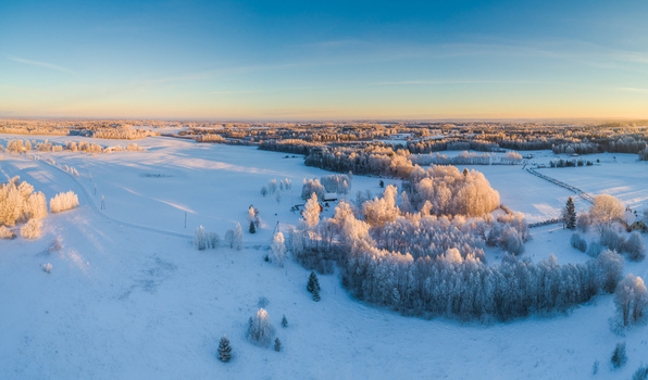 Aerial view of a snow covered rural landscape with frost covered trees and fields illuminated by the soft golden hour light in Latvia. Aerial view of a snow covered rural landscape with frost covered trees and fields illuminated by the soft golden hour light in Latvia.