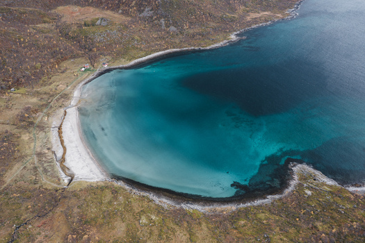 Aerial view of the turquoise waters of a coastal bay in Senja with rugged hills and rocky shoreline in Senja Troms Norway.