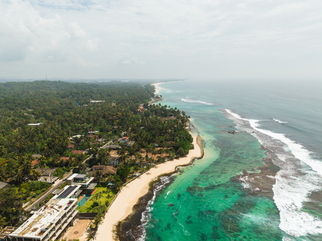 Aerial view of Thalpe Beach featuring turquoise waters white sand and lush palm trees along the coastline in Talpe Southern Province Sri Lanka. Aerial view of Thalpe Beach featuring turquoise waters white sand and lush palm trees along the coastline in Talpe Southern Province Sri Lanka.