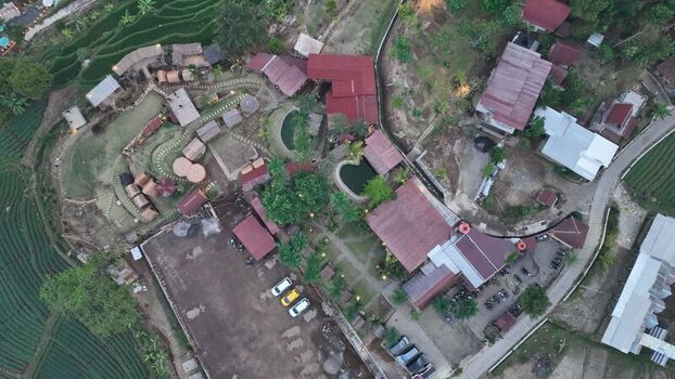 Aerial view of a resort in Trawas featuring small cabins a parking area and lush green rice terraces in the mountainous landscape of Trawas East Java Indonesia. Aerial view of a resort in Trawas featuring small cabins a parking area and lush green rice terraces in the mountainous landscape of Trawas East Java Indonesia.