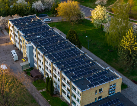 Aerial view of a multi story building with solar panels installed on the roof surrounded by green lawns and blooming trees in Vilnius County Lithuania. Aerial view of a multi story building with solar panels installed on the roof surrounded by green lawns and blooming trees in Vilnius County Lithuania.
