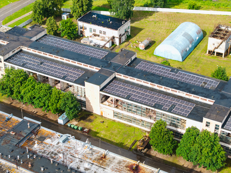 Aerial view of an industrial building featuring a large rooftop solar panel array surrounded by green trees and paved grounds in Olaine Olaine Municipality Latvia. Aerial view of an industrial building featuring a large rooftop solar panel array surrounded by green trees and paved grounds in Olaine Olaine Municipality Latvia.