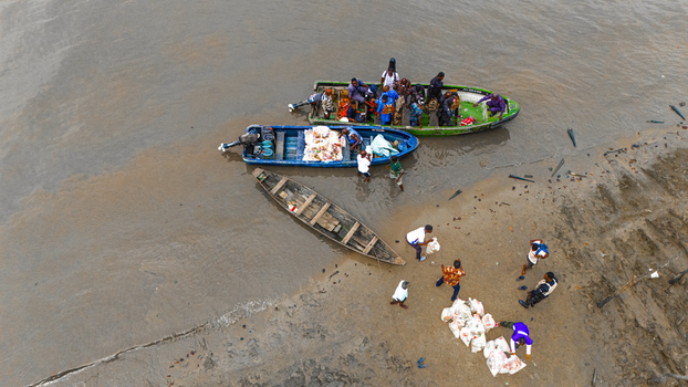 Aerial view of people unloading goods from small boats onto a muddy riverbank in Minima Rivers Nigeria.