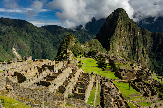 View of the ancient stone ruins of the Historic Sanctuary of Machu Picchu set against dramatic mountain peaks and lush green terraces in Urubamba Province Cusco Peru.