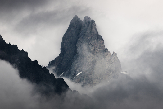 View of a sharp mountain peak emerging from thick grey clouds and mist in a moody atmosphere Aosta Valley Italy. View of a sharp mountain peak emerging from thick grey clouds and mist in a moody atmosphere Aosta Valley Italy.